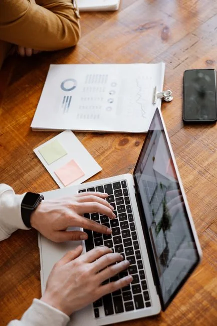 Hands typing on a laptop with cryptocurrency charts and smartphone display in view, focusing on digital finance.